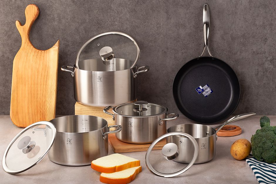 Premium stainless steel cookware set with wooden cutting board and vegetables.